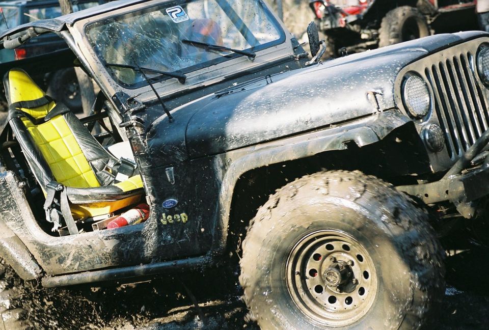 Mud-covered black Jeep CJ with yellow seats, front quarter view