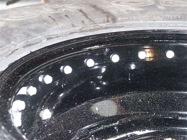 Close-up of a black metal rim with multiple white lug nut holes and a worn tire
