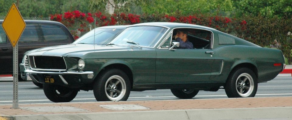 Green 1967 Ford Mustang Fastback driving next to a dark SUV