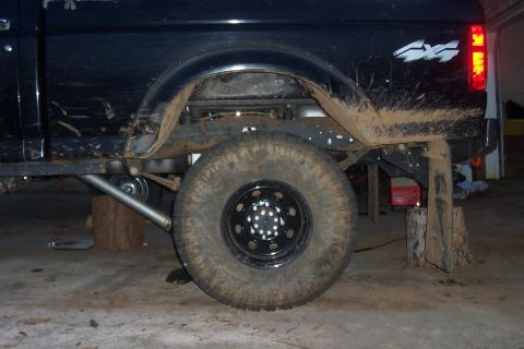 1994 Ford F-150 - The rear suspension and wheel of a dirty pickup truck are visible, supported by wooden blocks.