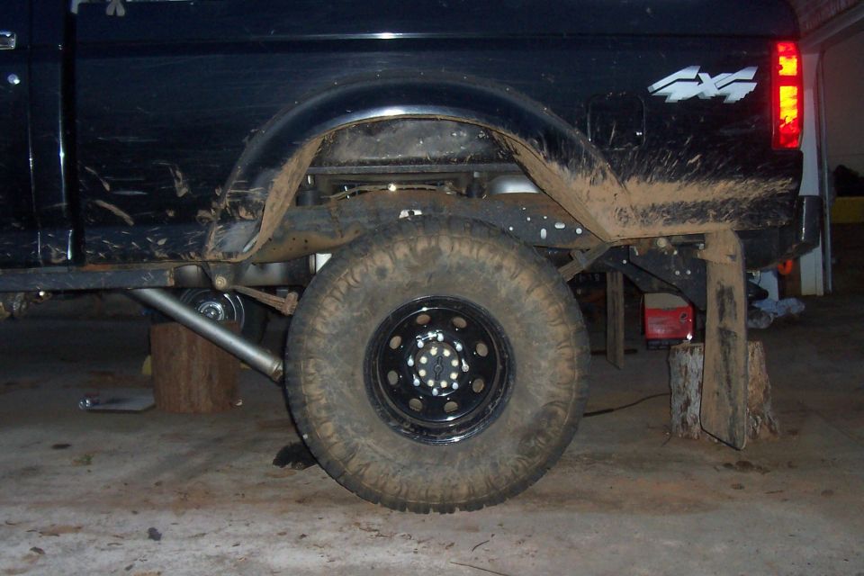 Pickup truck's rear wheel and suspension, lifted on blocks. Mud splattered