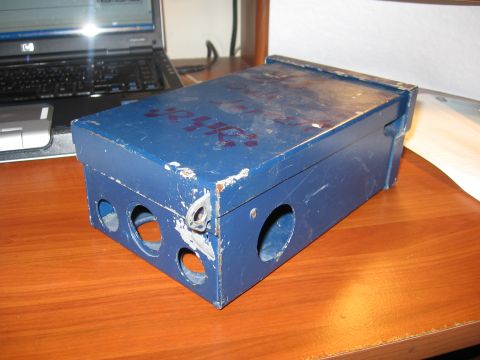 1974 Ford F-100 - A blue metal box with some red markings on top sits on a wooden surface next to a laptop computer.
