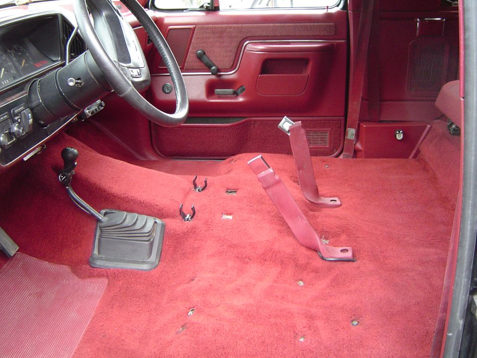 Ford truck cab with seat removed showing red carpet, door panels, and floor shifter