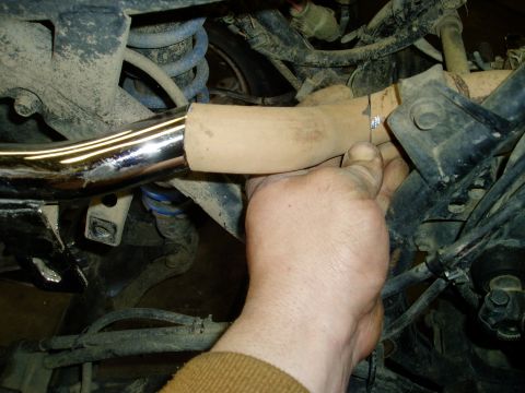 2000 Ford E350 - A mechanic works on an exhaust pipe, with suspension components and wiring visible in the background.