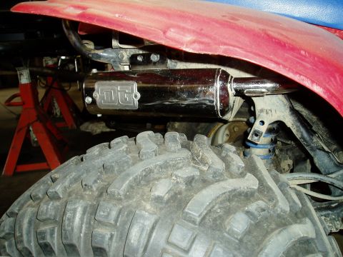 2000 Ford E350 - Detail shot of an ATV's exhaust system and large tire, with red body panels overhead.