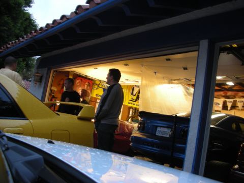 1992 Ford Crown Victoria - A blue coupe with a spoiler and a visible license plate is parked in a garage, with other vehicles and people present.