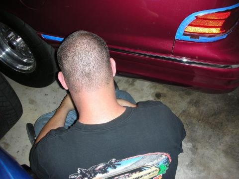 1992 Ford Crown Victoria - A person sits near the rear of a red 1992 Ford Crown Victoria, with blue tape applied to the taillight assembly.