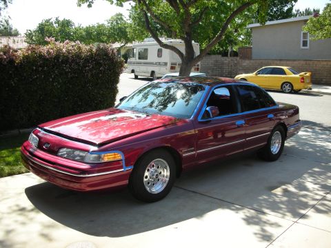 1992 Ford Crown Victoria - A maroon Ford Crown Victoria is parked in a driveway with its hood open, while a yellow sedan is visible on the street.
