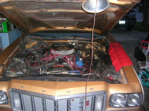 1975 Ford Ranchero - The engine bay of a 1975 Ford Ranchero is open, revealing the V8 engine with red spark plug wires and a chrome air cleaner.