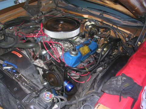 1975 Ford Ranchero - The engine bay of a gold 1975 Ford Ranchero shows a V8 engine with an air filter, distributor, and numerous wires and hoses.