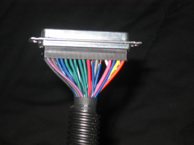 Close-up of a multi-pin electrical connector with a bundle of colorful wires emerging from black corrugated tubing