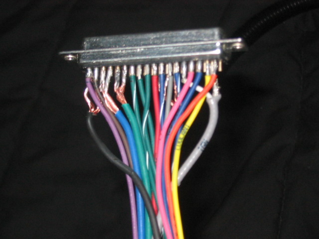 Close-up of a silver electrical connector with many colored wires soldered to its pins
