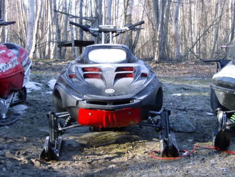 1982 Chevrolet C/K Pickup - Three snowmobiles are parked in a muddy, wooded area with snow on the ground.
