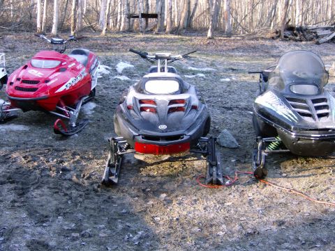 1982 Chevrolet C/K Pickup - Three snowmobiles are parked outdoors in a wooded area, with a watermark at the bottom right.