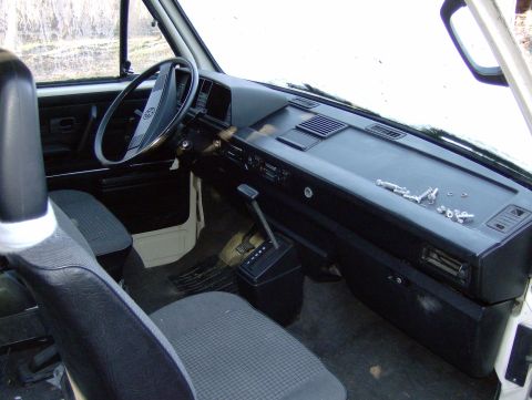 1982 Chevrolet C/K Pickup - The interior of a van is visible, including the dashboard, steering wheel, and seats, with loose parts on the dash.