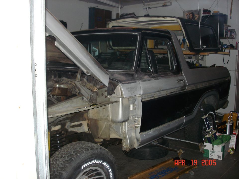 Ford Bronco with hood open, undergoing repairs in a garage. Another vehicle is visible behind it