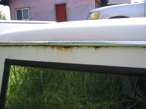 1968 Ford Bronco - Rust is visible along the chrome trim of a white vehicle's roofline, with another vehicle in the background.