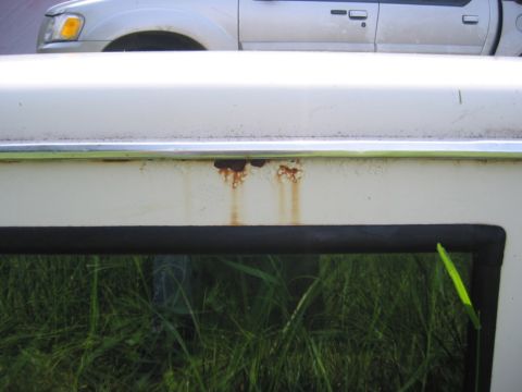 1968 Ford Bronco - Rust stains drip down the side of a white vehicle, with a silver SUV parked behind it.