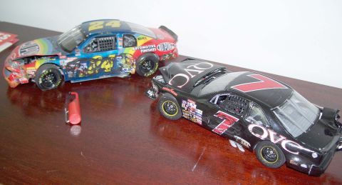 1971 Ford Ranchero - Two toy race cars, one with rainbow graphics and the other black with the number 7, sit on a wooden surface, both appearing damaged.