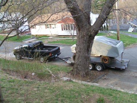 1995 Ford Bronco - A black pickup truck is seen towing a trailer with a covered object on a residential street.