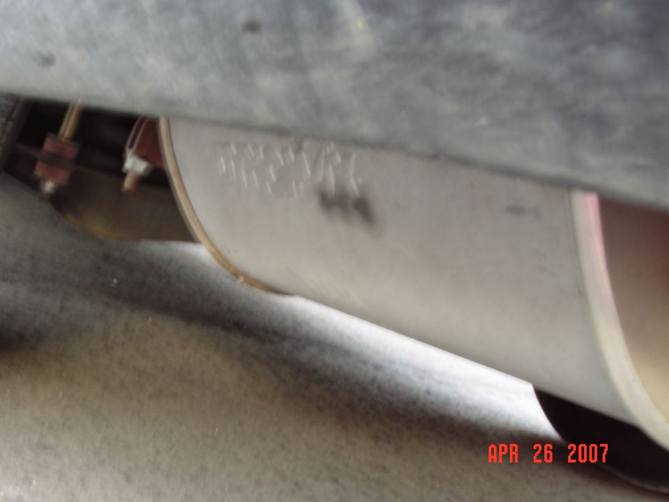 Underbody shot of a silver aftermarket muffler with stamped logo and rusty hanger bracket, dated APR 26 2007
