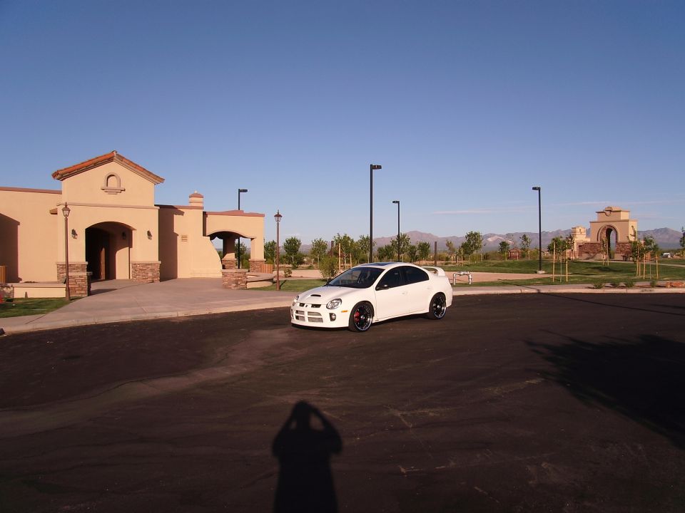 White Dodge Neon SRT-4 parked in front of a building with a shadow of the photographer in the foreground