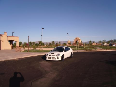 1996 Ford Probe - A white Dodge Neon SRT-4 is parked in a lot with buildings and mountains in the background.