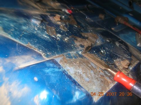 1991 Ford F-150 - This image shows a close-up of a blue metal surface with significant rust and debris, along with a chisel tool.