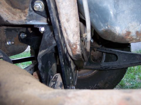 1996 Ford Bronco - Underbody view looking outward past a black steel bracket bolted to the frame rail with fresh zinc-plated hardware, alongside a surface-rus…