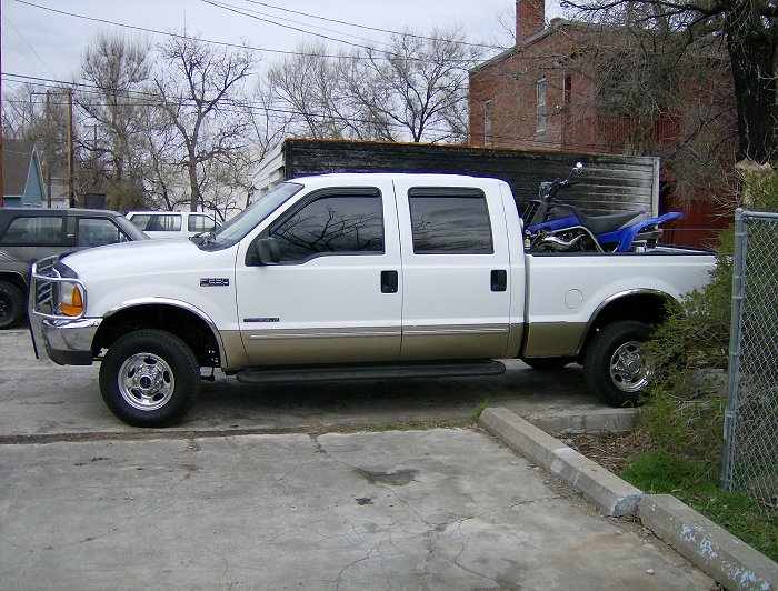 White and tan 2000 Ford F-250 crew cab pickup truck side view with a dirt bike in the bed