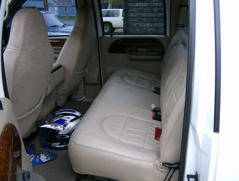 2000 Ford F-250 - The rear interior of a truck shows tan leather seats and a helmet on the floor.