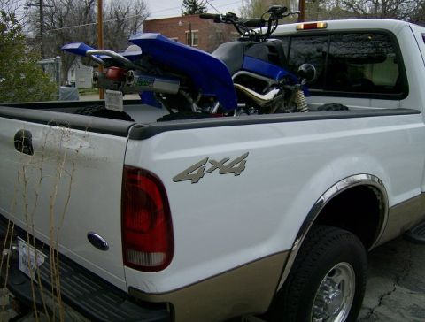 2000 Ford F-250 - A white pickup truck is shown from the rear with a blue ATV loaded in its bed.