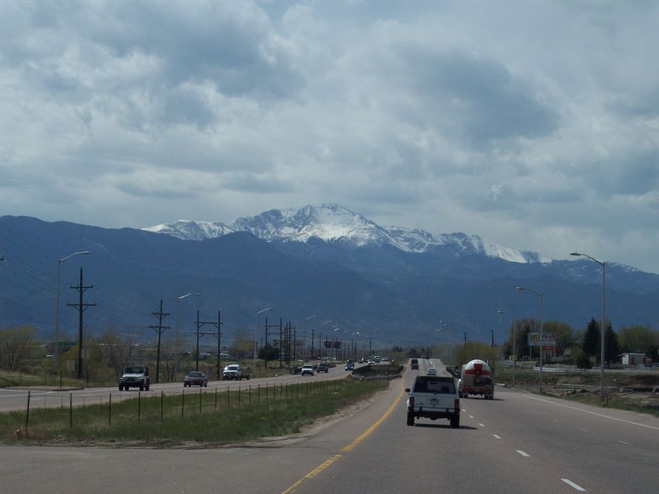 Cars on a highway with snow-capped mountains in the distance under a cloudy sky