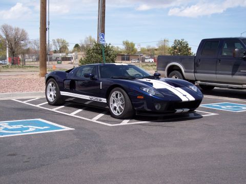 1972 Ford Ranchero - A blue Ford GT with white racing stripes is parked in a handicapped parking space next to a dark pickup truck.
