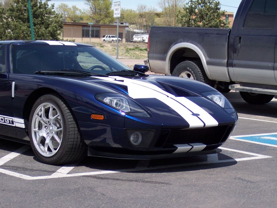 Blue Ford GT sports car with white racing stripes parked next to a pickup truck