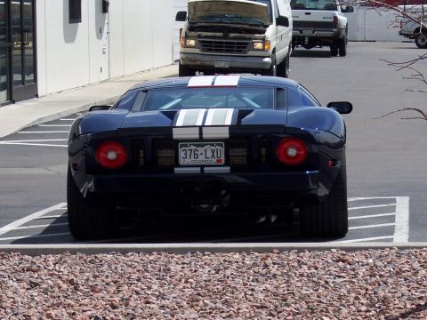 1972 Ford Ranchero - A dark blue Ford GT with racing stripes is parked in a lot, with vans and a truck behind it.