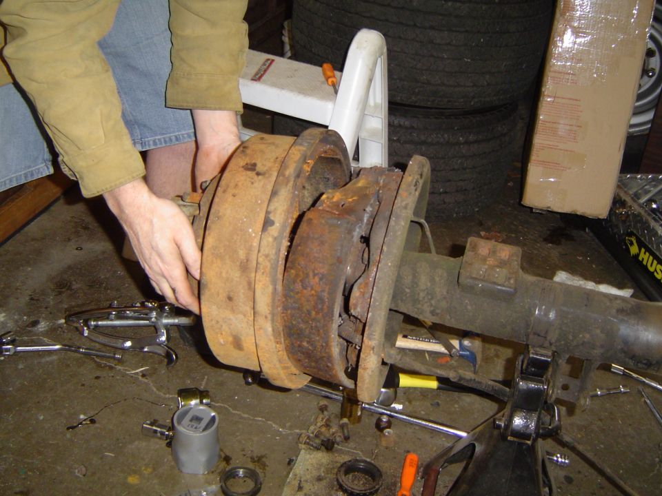 Rusty brake drum assembly on a vehicle axle, being worked on by a person