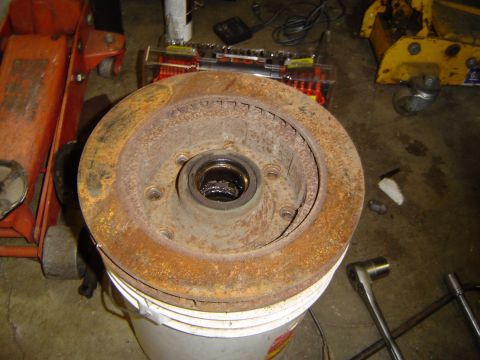1978 Ford Bronco - A heavily rusted brake rotor and hub assembly is shown, resting on a bucket with various tools nearby.
