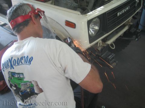 1987 Suzuki Samurai - A mechanic grinds sparks off the front fender of a white Suzuki Samurai, likely during a shock swap modification.