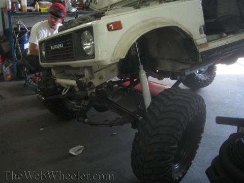 1987 Suzuki Samurai - A mechanic works on the front suspension of a Suzuki Samurai, which has been modified with large off-road tires.