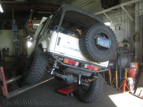 1987 Suzuki Samurai - A white 1987 Suzuki Samurai is shown on a lift in a garage, with another vehicle above it.