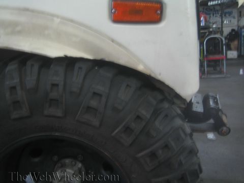 1987 Suzuki Samurai - Close-up of a white SUV's fender and tire, showing an orange marker light and a heavy-duty tread pattern.