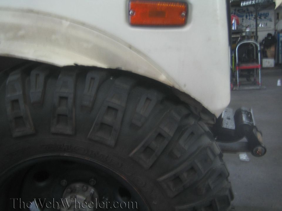 White SUV fender with orange marker light above a large off-road tire