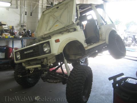 1987 Suzuki Samurai - A white 1987 Suzuki Samurai is shown with its hood up and suspension lifted, large off-road tires.