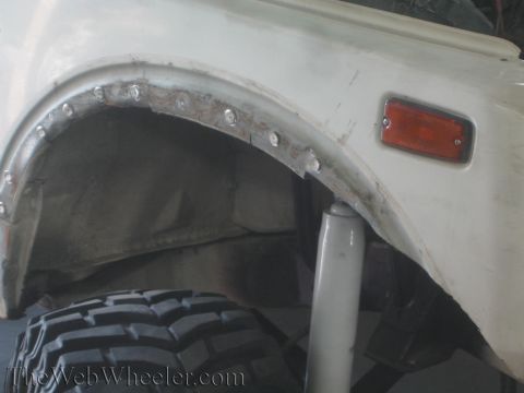 1987 Suzuki Samurai - Close-up of the wheel well on a 1987 Suzuki Samurai, showing an aftermarket shock absorber and a large off-road tire.