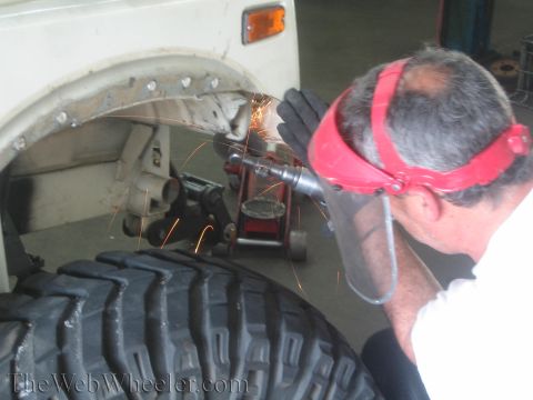 1987 Suzuki Samurai - A person is using a grinder to modify the wheel well of a vehicle, with a large tire visible.