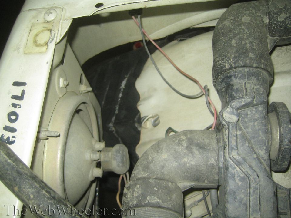 Close-up of engine bay with a headlight assembly and some plumbing parts. Some handwritten text is visible on the white panel