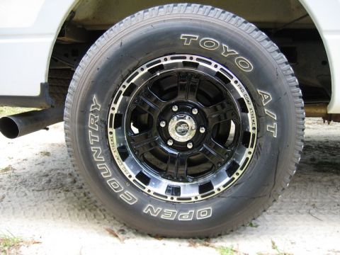 2004 Ford F-150 - Close-up of a black aftermarket wheel and TOYO Open Country A/T tires mounted on a white truck.