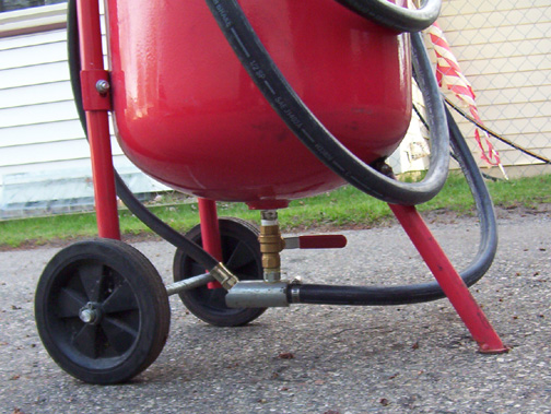 Red sandblaster tank with black wheels and hoses