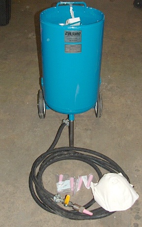 1965 Ford Mustang - A blue sandblaster tank with a coiled hose and various nozzles is shown on a concrete floor.